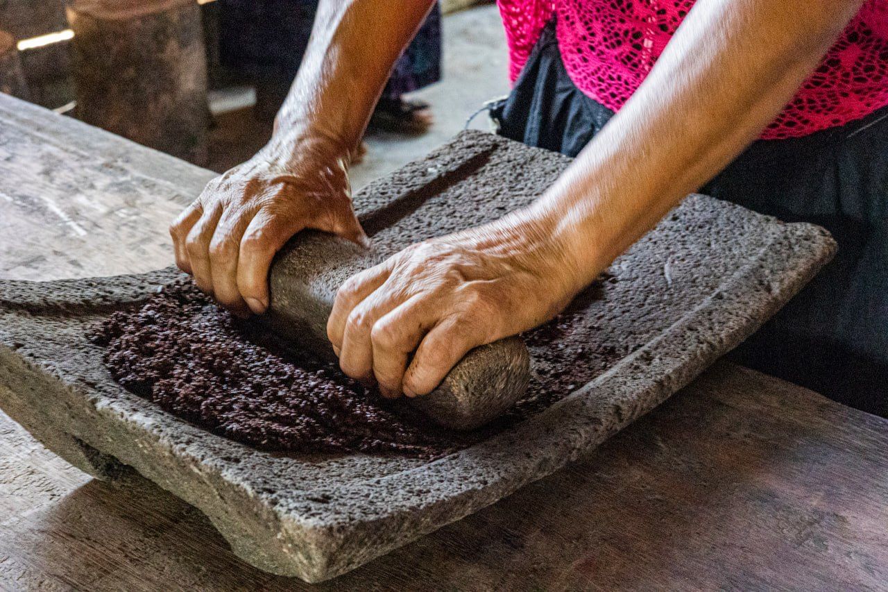 Traditionelles Mahlen von Kakaobohnen auf einer Steinmühle (Metate) – schonende Kaltverarbeitung erhält hitzeempfindliche Pflanzenstoffe und Aromen